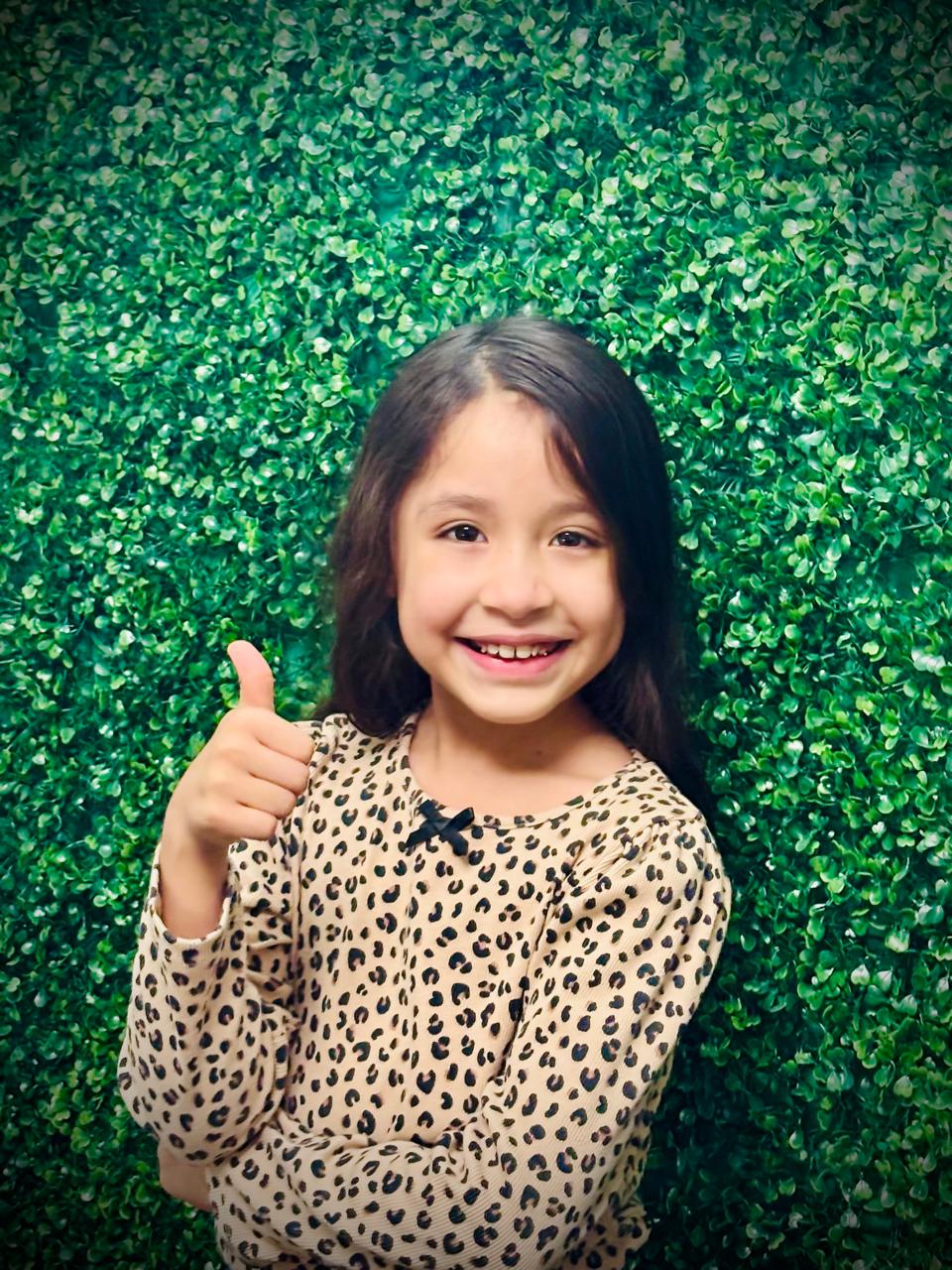 Niña paciente dando pulgar arriba frente al muro verde del consultorio Especialidades Dentales