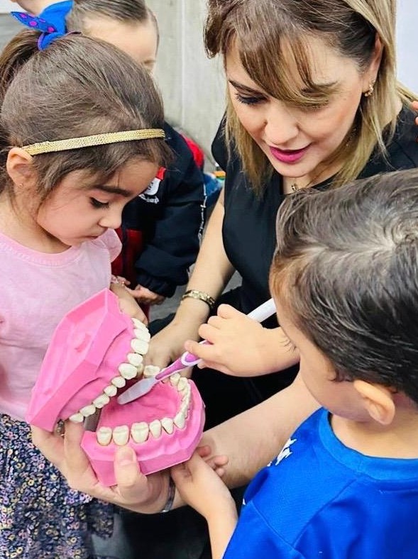 Dra. Yadira Garza enseñando técnicas de cepillado a niños con modelo dental gigante en charla educativa escolar en Monterrey